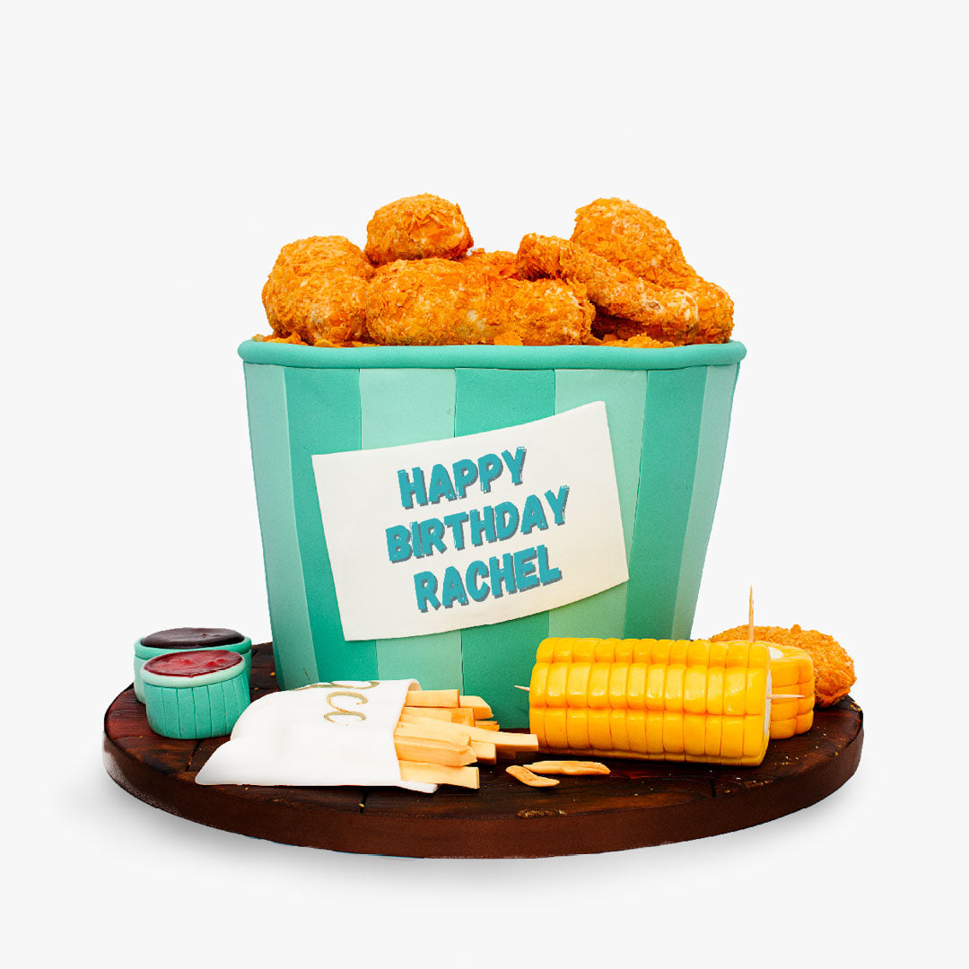 Fried chicken-themed birthday cake featuring a bucket filled with edible chicken pieces, fries, corn on the cob and dipping sauces