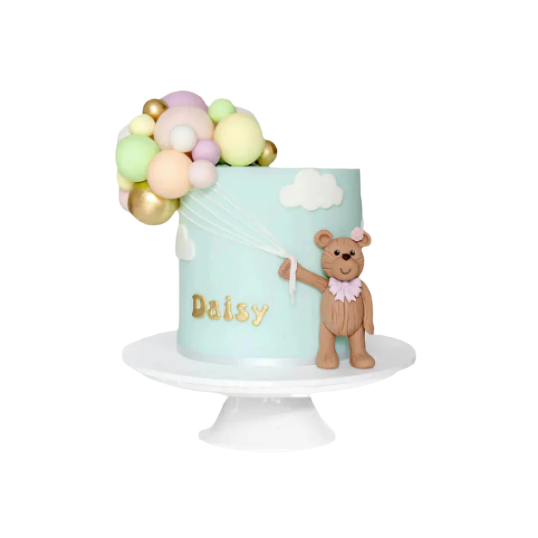 Birthday cake with a cluster of colourful balloons and a teddy bear holding onto balloon strings