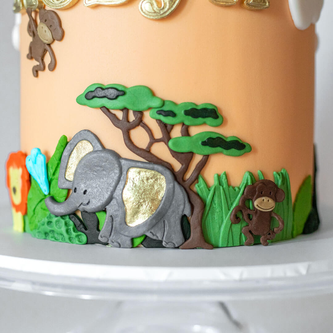 Fun childrens animal birthday cake featuring a colourful safari scene with jungle animals, personalised with age and name handpainted in gold