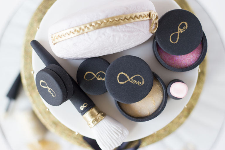 Black and gold makeup cake with gold glitter and quilting decorations. Two tiered cake with edible fondant lipstick, eye shadow palette, mirror, mini makeup bag, makeup brush and nail polish
