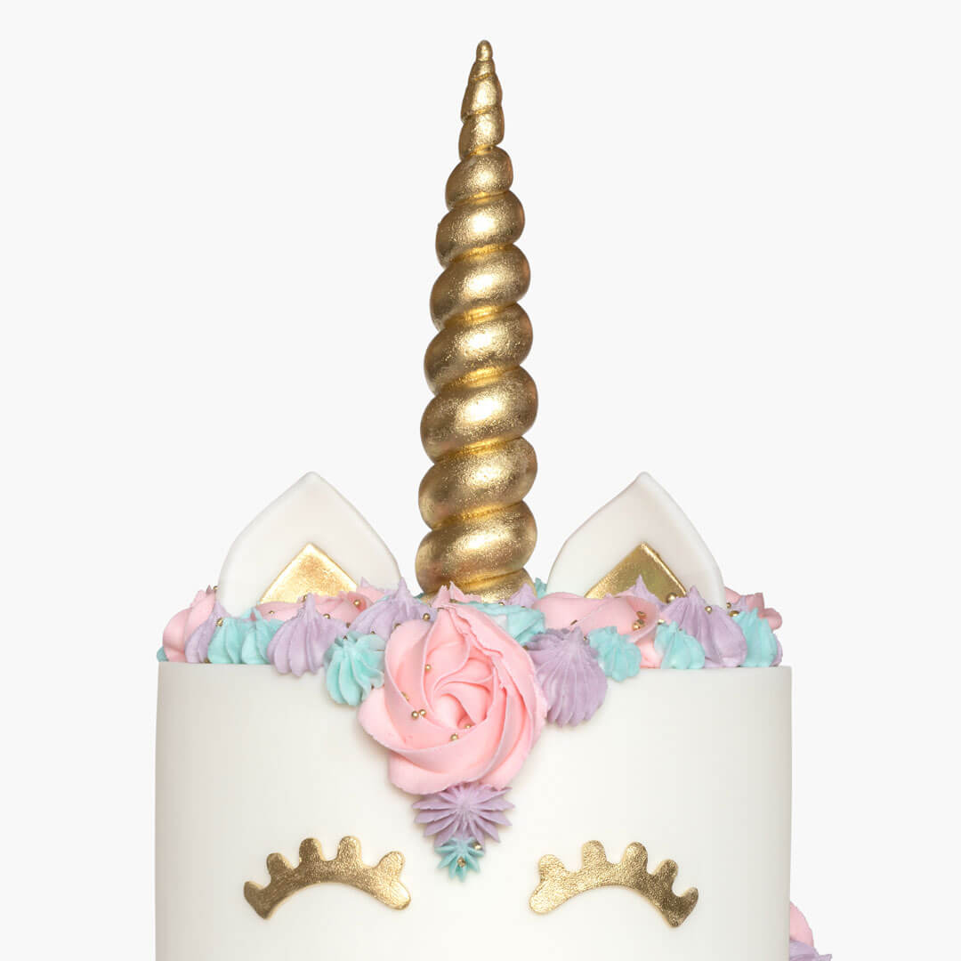 Child's unicorn cake with a pastel coloured buttercreams, gold sugar horn, fondant ears and closed eyes with lashes