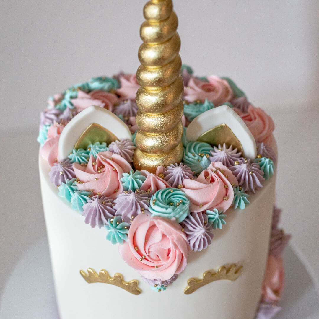 Child's unicorn cake with a pastel coloured buttercreams, gold sugar horn, fondant ears and closed eyes with lashes