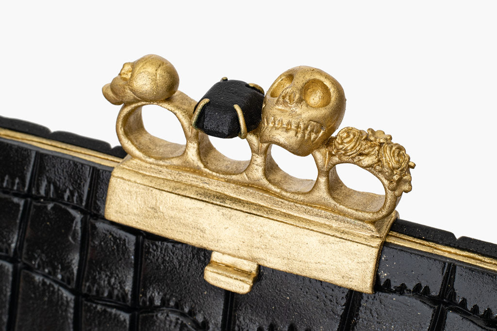Alexander McQueen knuckle clutch handbag cake. The handbag cake is enveloped in a black fondant leather-like shiny finish. Finished with gold knuckle rings on top.