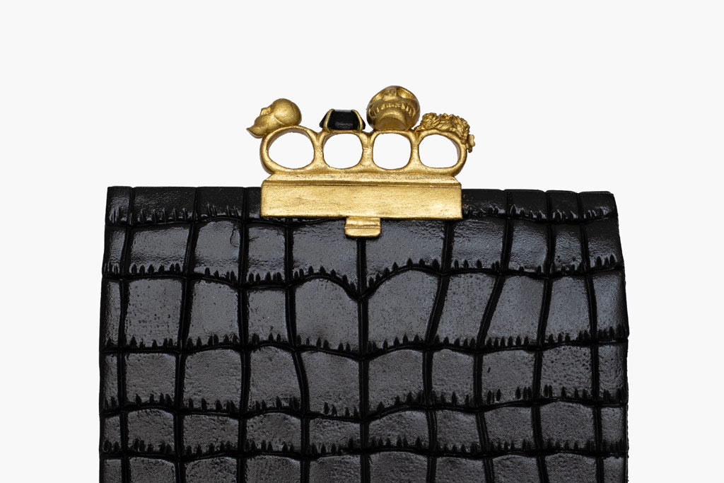Alexander McQueen knuckle clutch handbag cake.  The handbag cake is enveloped in a black fondant leather-like shiny finish. Finished with gold knuckle rings on top.