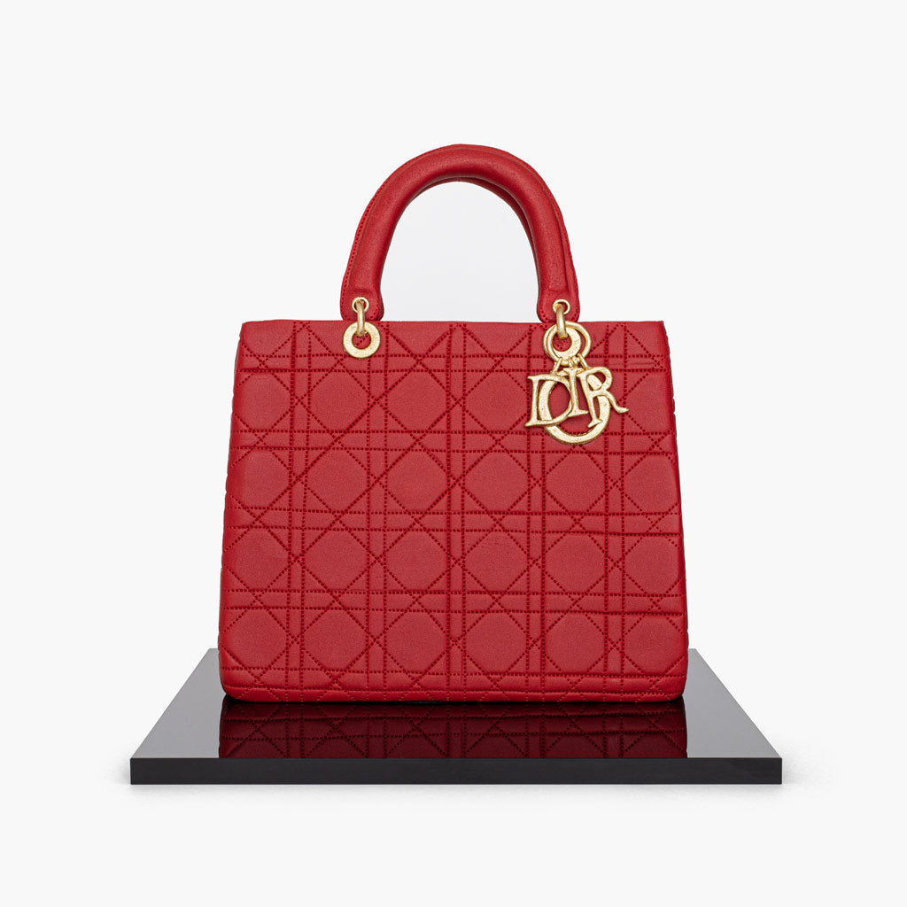 Timeless Dior Lady bag in edible format. This red handbag cake is delicious, light and moist and covered in a rich ruby red fondant with flawless stitching, perfectly replicating the signature Dior colour palette. With quilted textures and hand-painted gold Dior charms, this edible handbag cake has an incredibly realistic finish.