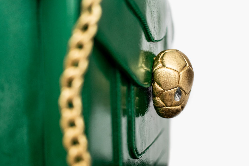 This Bulgari handbag cake is a luxurious creation that combines cake artistry and decadence. The handbag cake is covered in deep green fondant icing then pearlised to resemble the sheen on the original Serpenti bag. The realistic gold chain, precision stitch work and detailed hand-sculpted Serpenti snake head clasp are all works of art.
