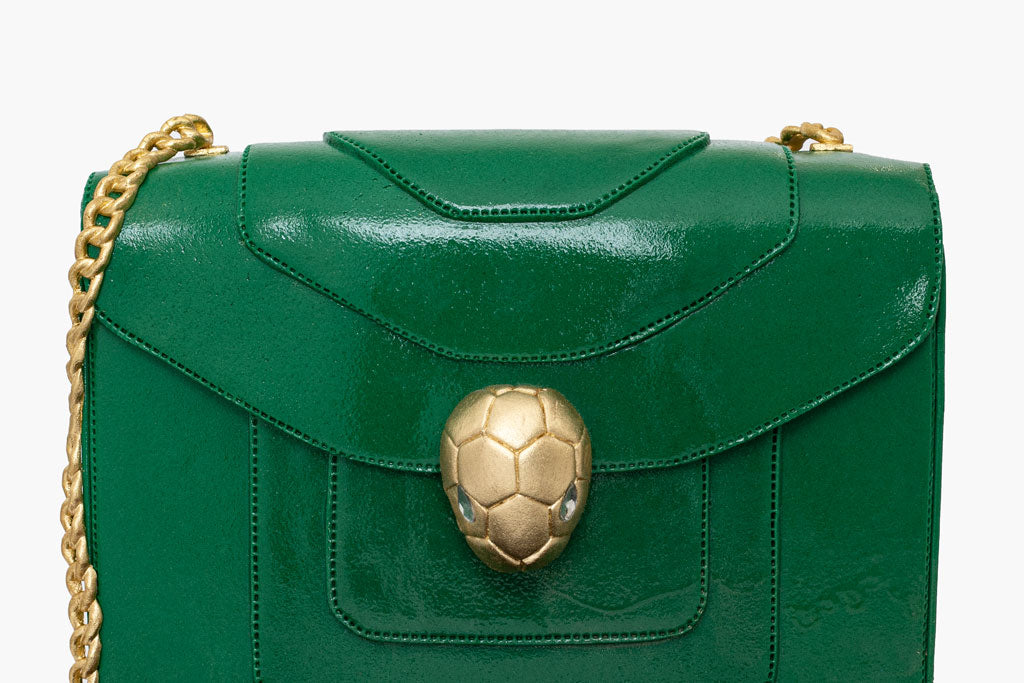 This Bulgari handbag cake is a luxurious creation that combines cake artistry and decadence. The handbag cake is covered in deep green fondant icing then pearlised to resemble the sheen on the original Serpenti bag. The realistic gold chain, precision stitch work and detailed hand-sculpted Serpenti snake head clasp are all works of art.