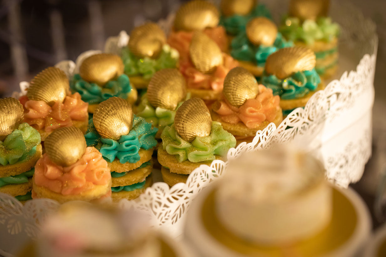 stacks of cookies with colourful icing topped with edible gold painted shells