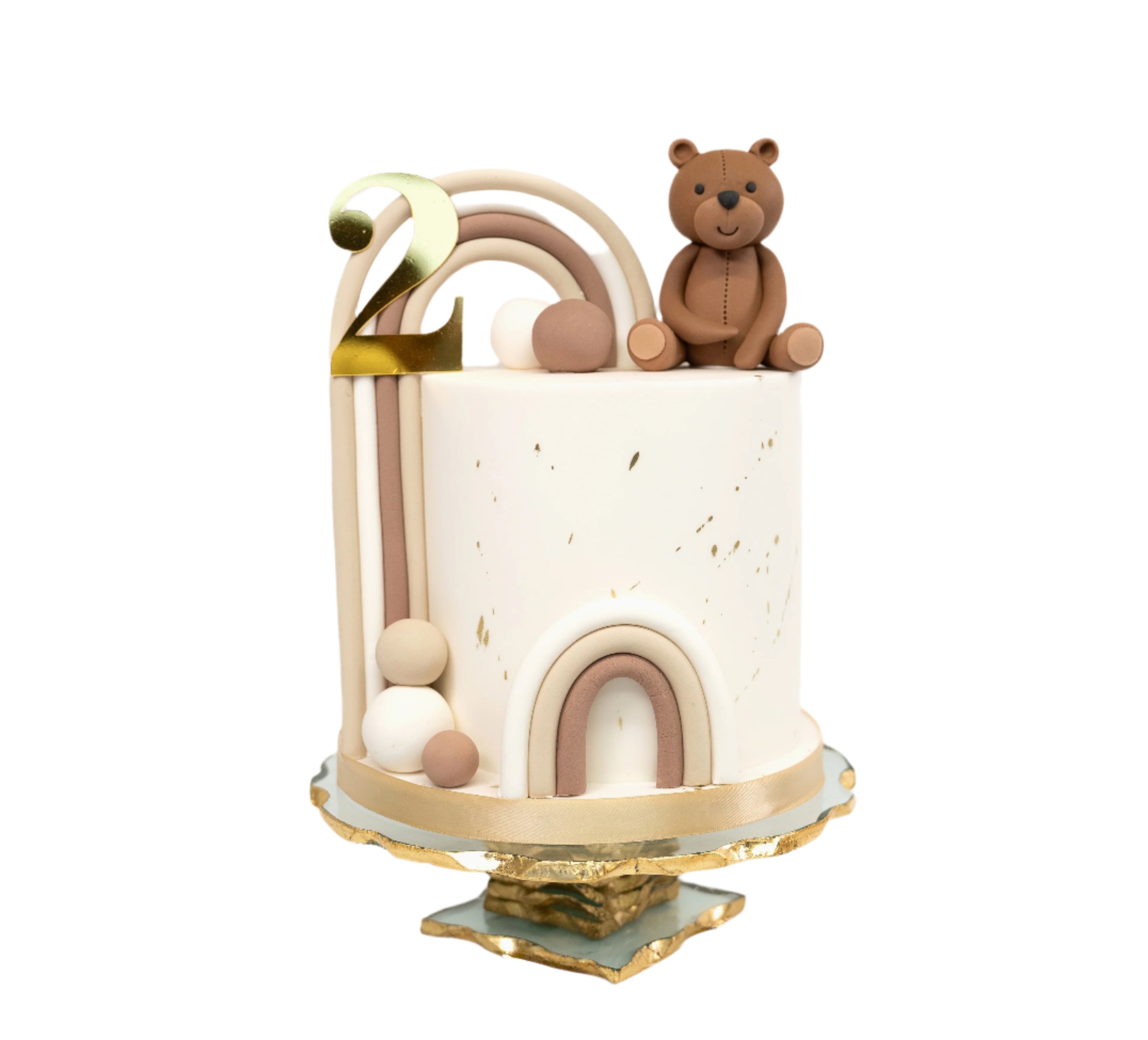 Elegant 2nd birthday cake with a handmade teddy bear topper, gold acrylic number "2", neutral toned rainbows, with gold-speckled design.