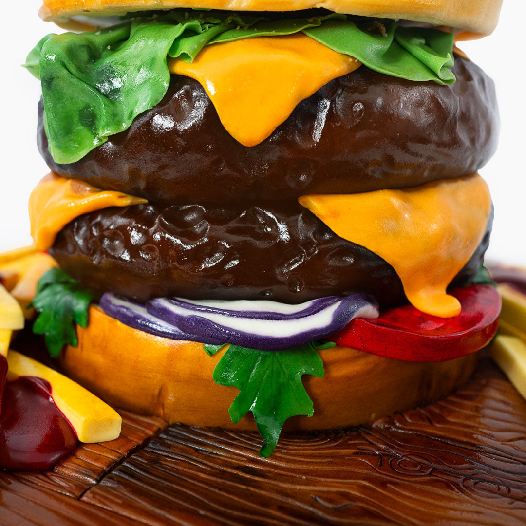 Novelty Burger cake with all the trimmings including cheese, lettuce, red onions and chips, sandwiched between a sesame seeded bun