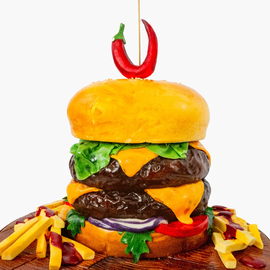 Novelty Burger cake with all the trimmings including cheese, lettuce, red onions and chips, sandwiched between a sesame seeded bun