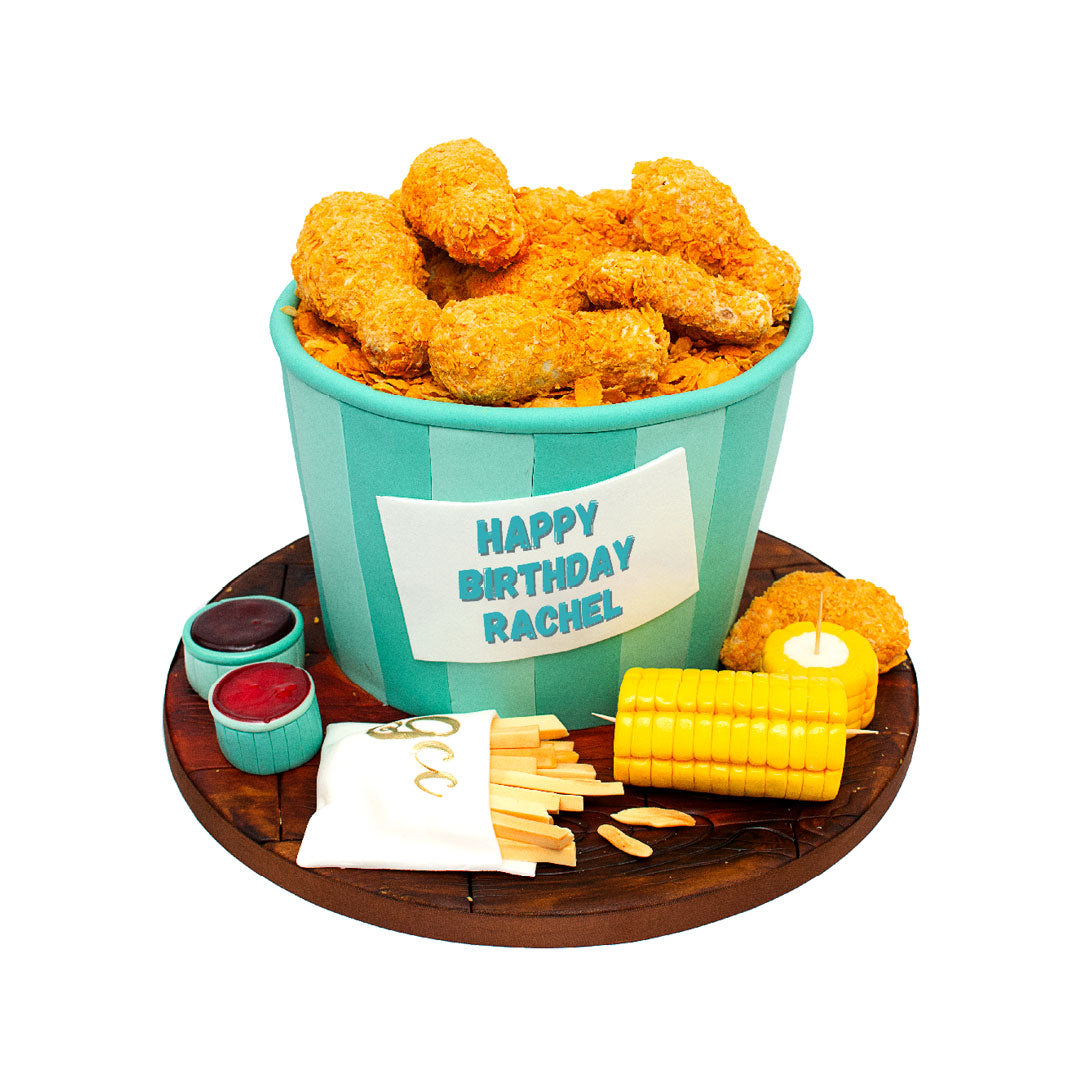 Fried chicken-themed birthday cake featuring a bucket filled with edible chicken pieces, fries, corn on the cob and dipping sauces