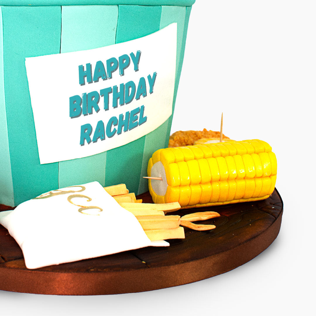 Fried chicken-themed birthday cake featuring a bucket filled with edible chicken pieces, fries, corn on the cob and dipping sauces