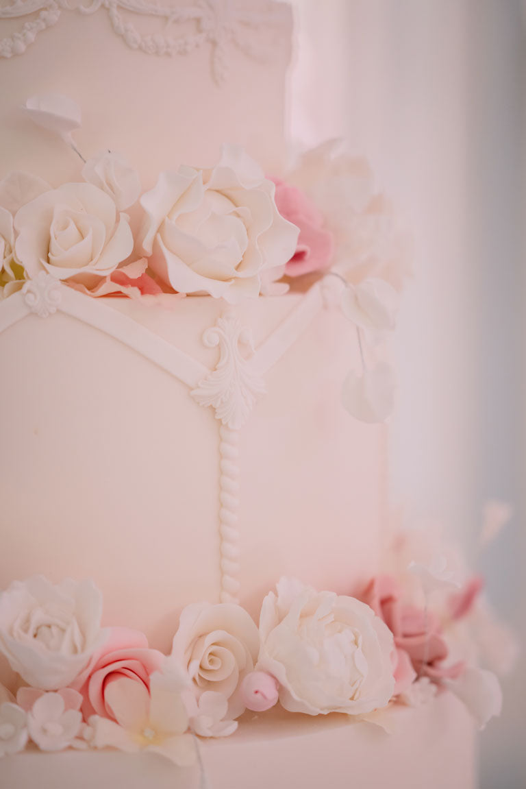 side of a beautiful pale pink wedding cake detailed with white and pink icing flowers