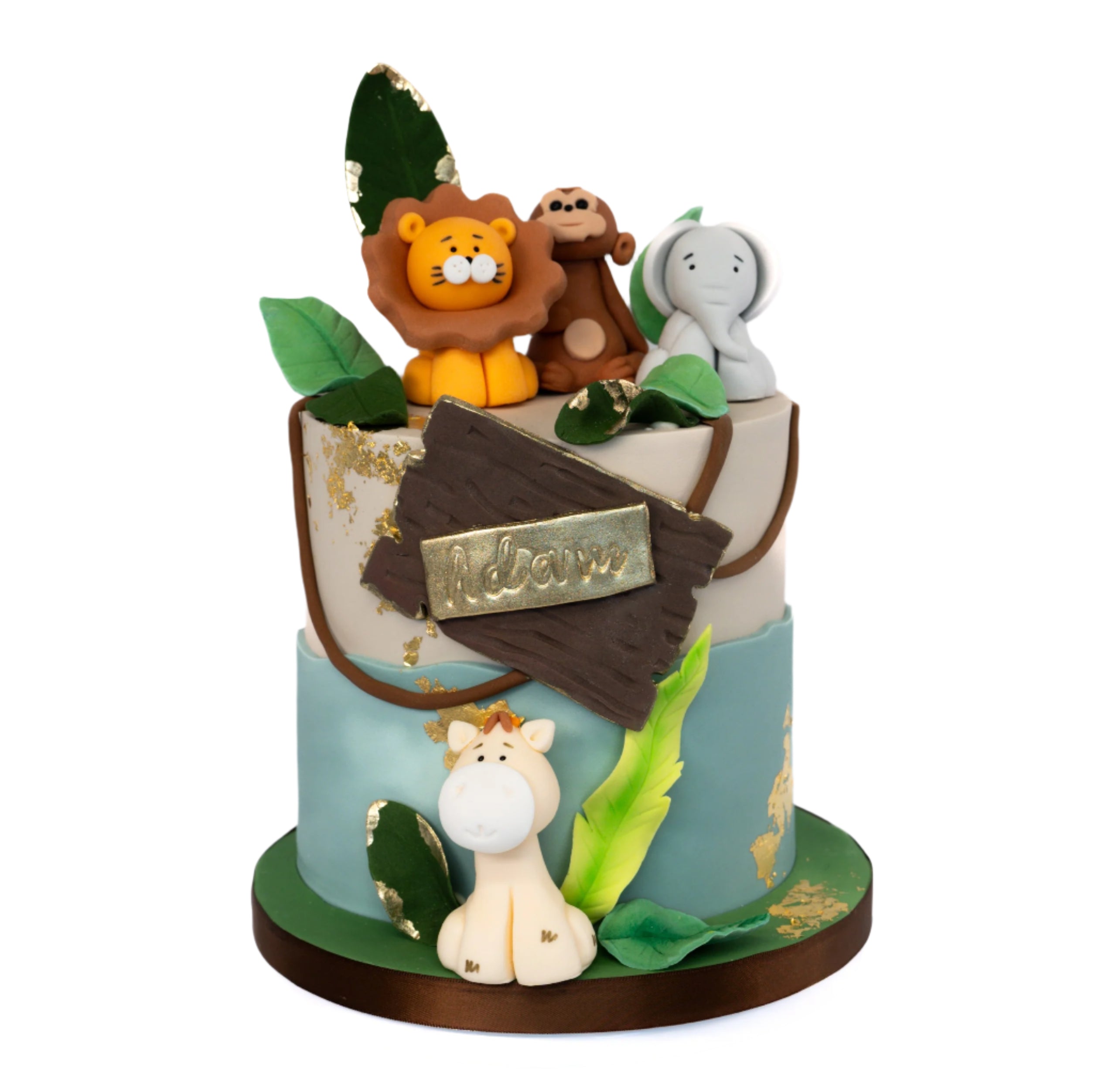 A whimsical jungle-themed cake decorated with fondant animals (kion monkey, elephant, gifaffe) green leaves, gold leaf accents and a wooden-style personalised name plaque