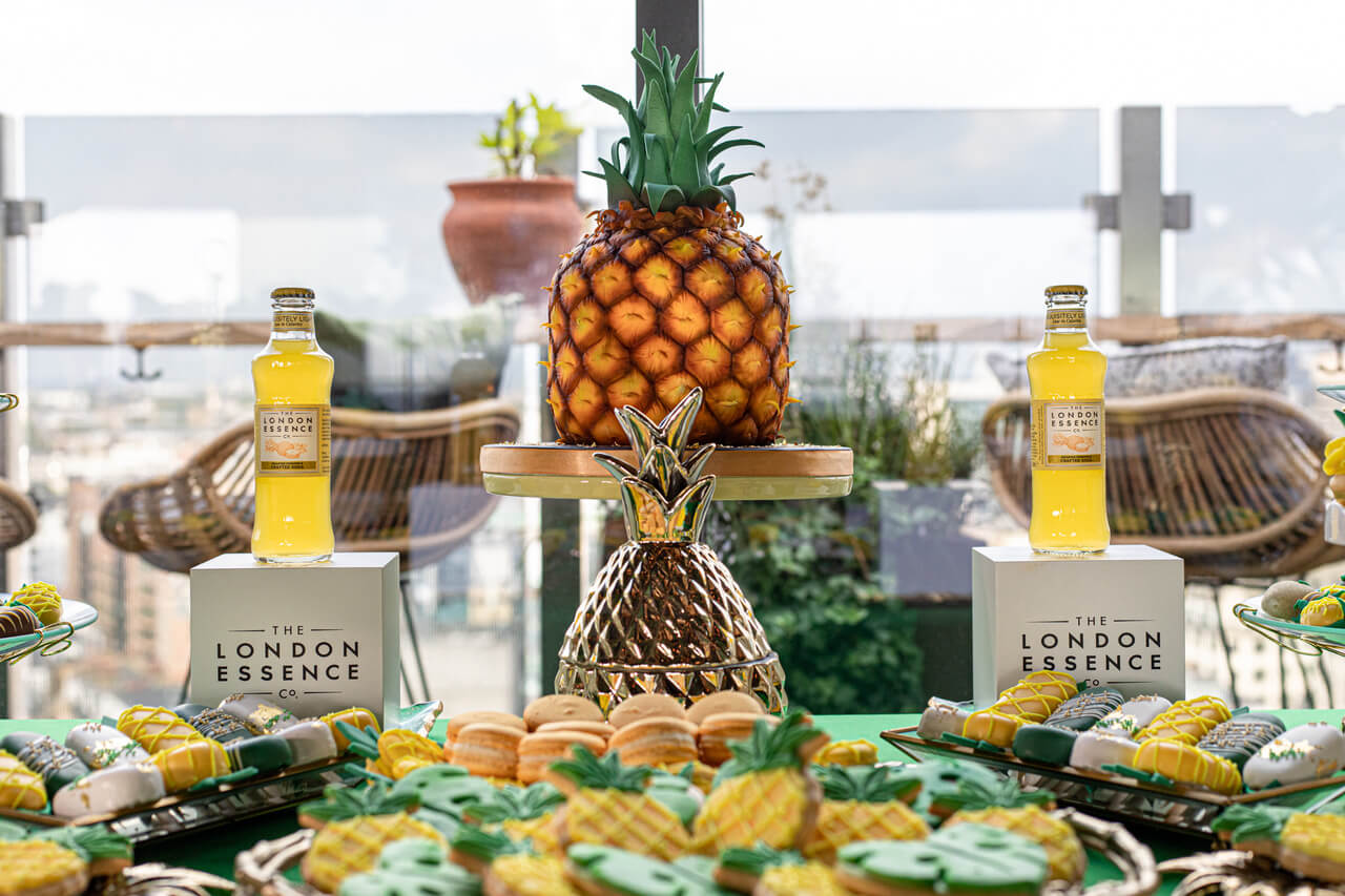 a colourful pineapple shaped cake on top of a cake stand surrounded by cookies and lollies in the same theme