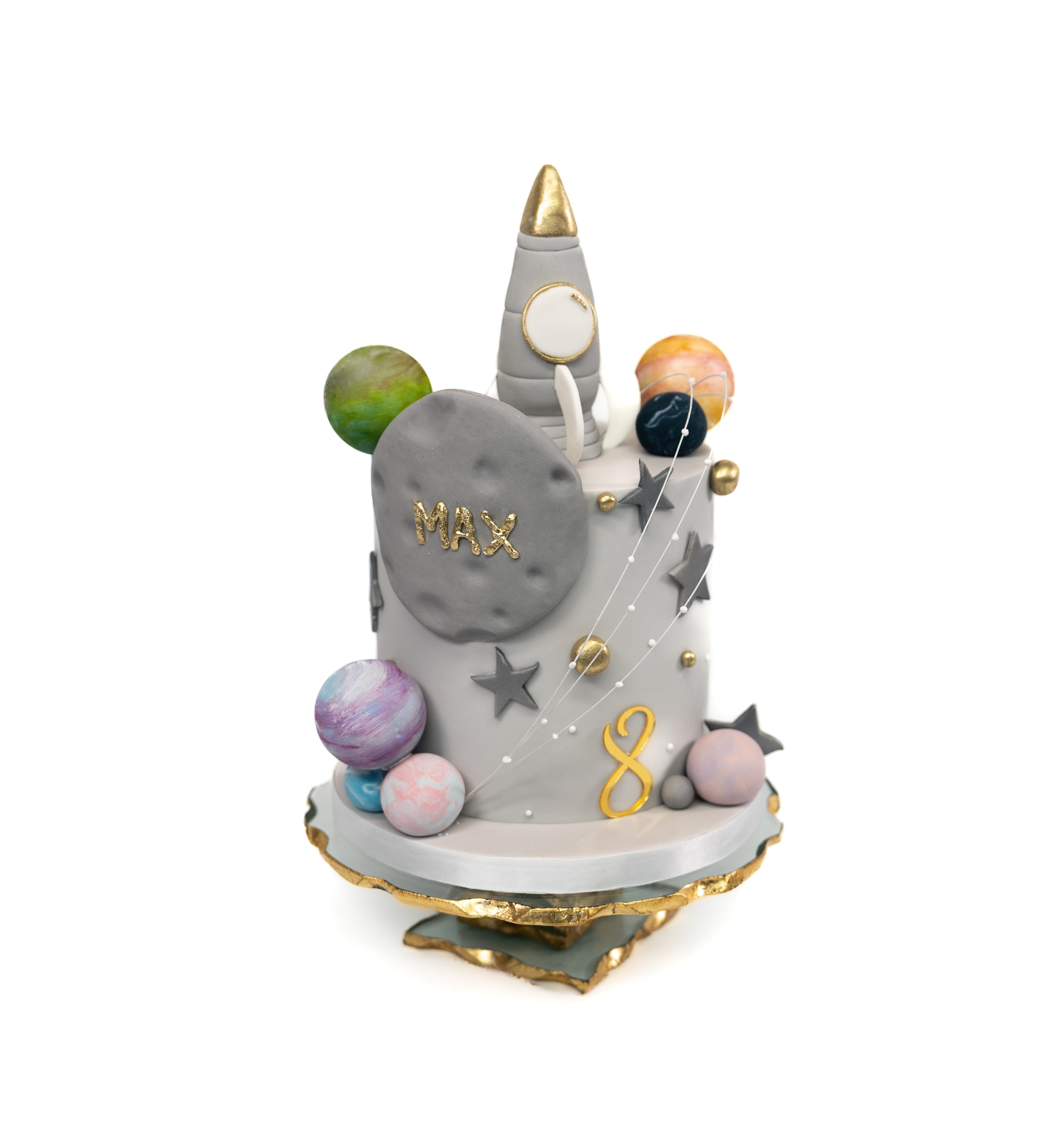 A space-themed cake showcasing a silver rocket ship with edible stars and planets, personalised with name and acrylic age