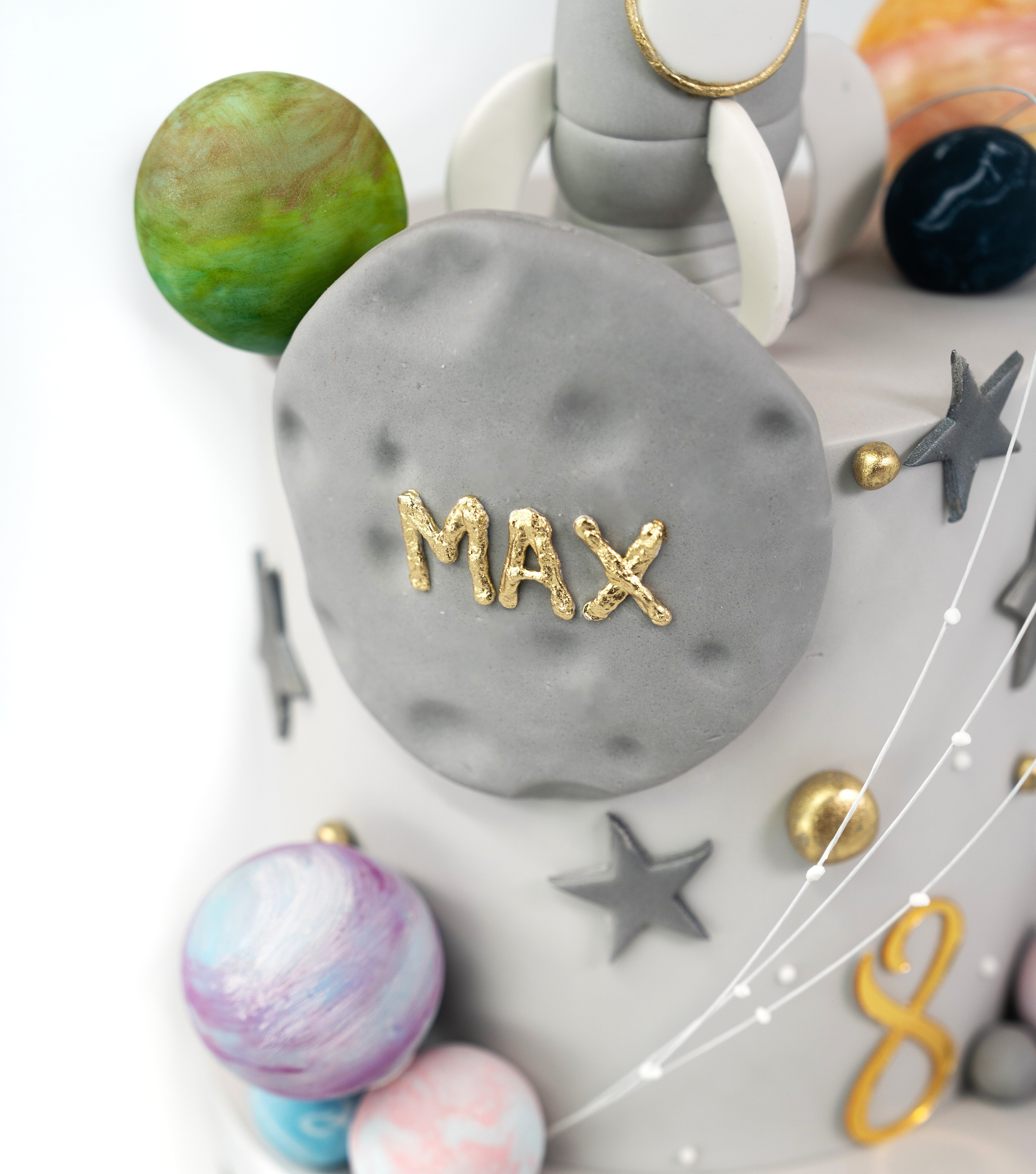 A space-themed cake showcasing a silver rocket ship with edible stars and planets, personalised with name and acrylic age