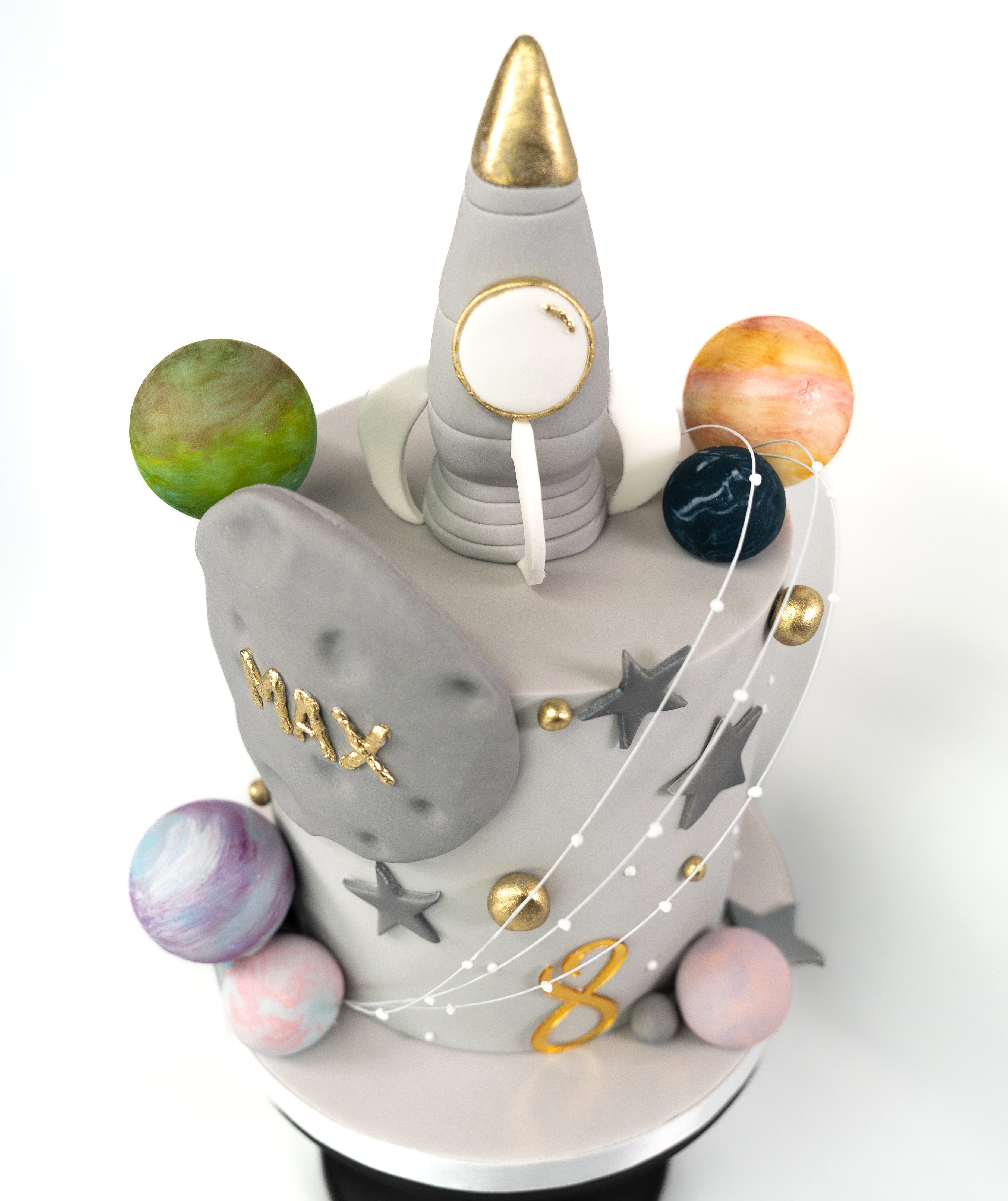 A space-themed cake showcasing a silver rocket ship with edible stars and planets, personalised with name and acrylic age