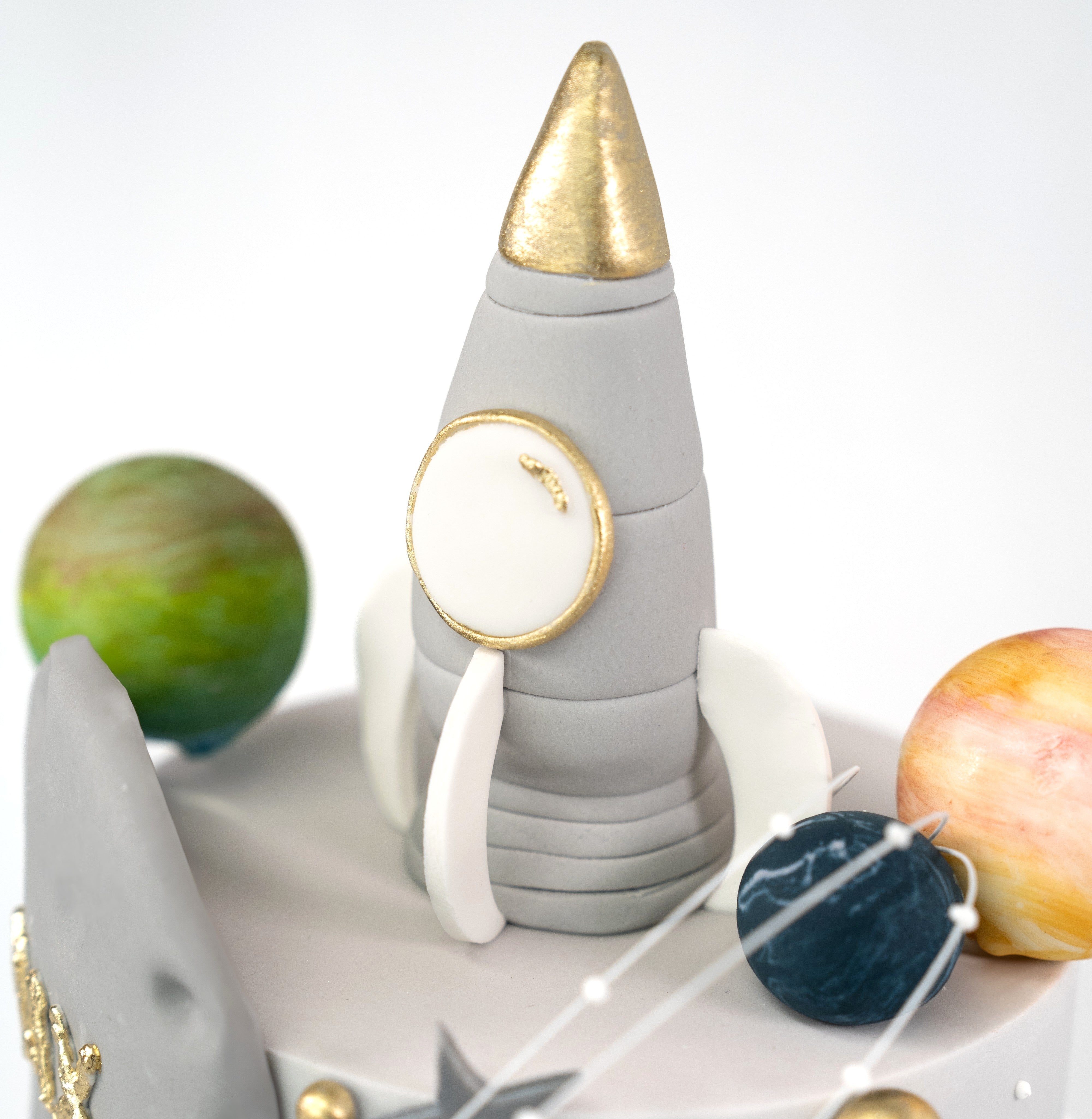 A space-themed cake showcasing a silver rocket ship with edible stars and planets, personalised with name and acrylic age