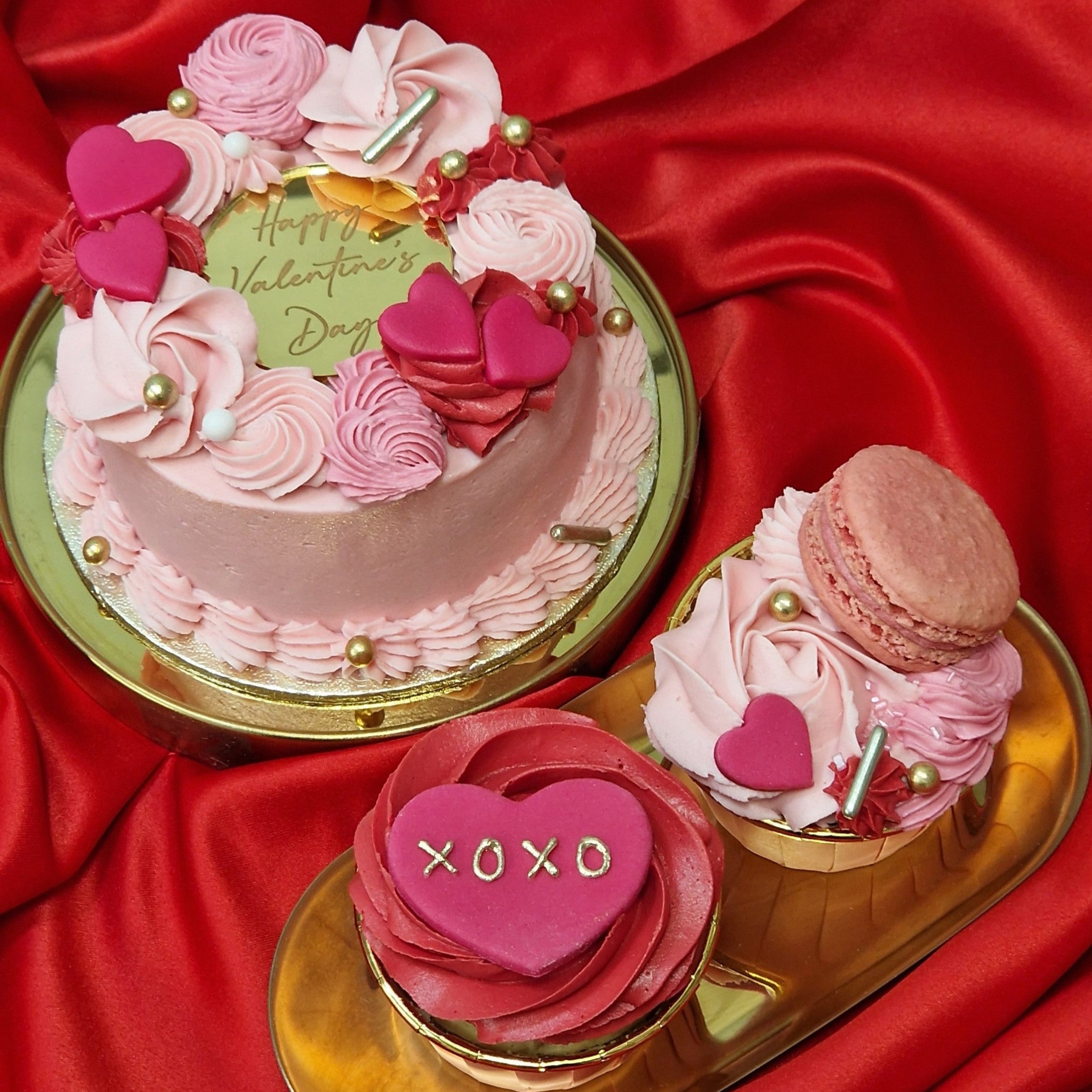 Valentine's Bento Box featuring a pink buttercream mini cake with heart decorations and buttercream swirls, accompanied by 2 cupcakes decorated with macaron, fondant hearts and gold sprinkles