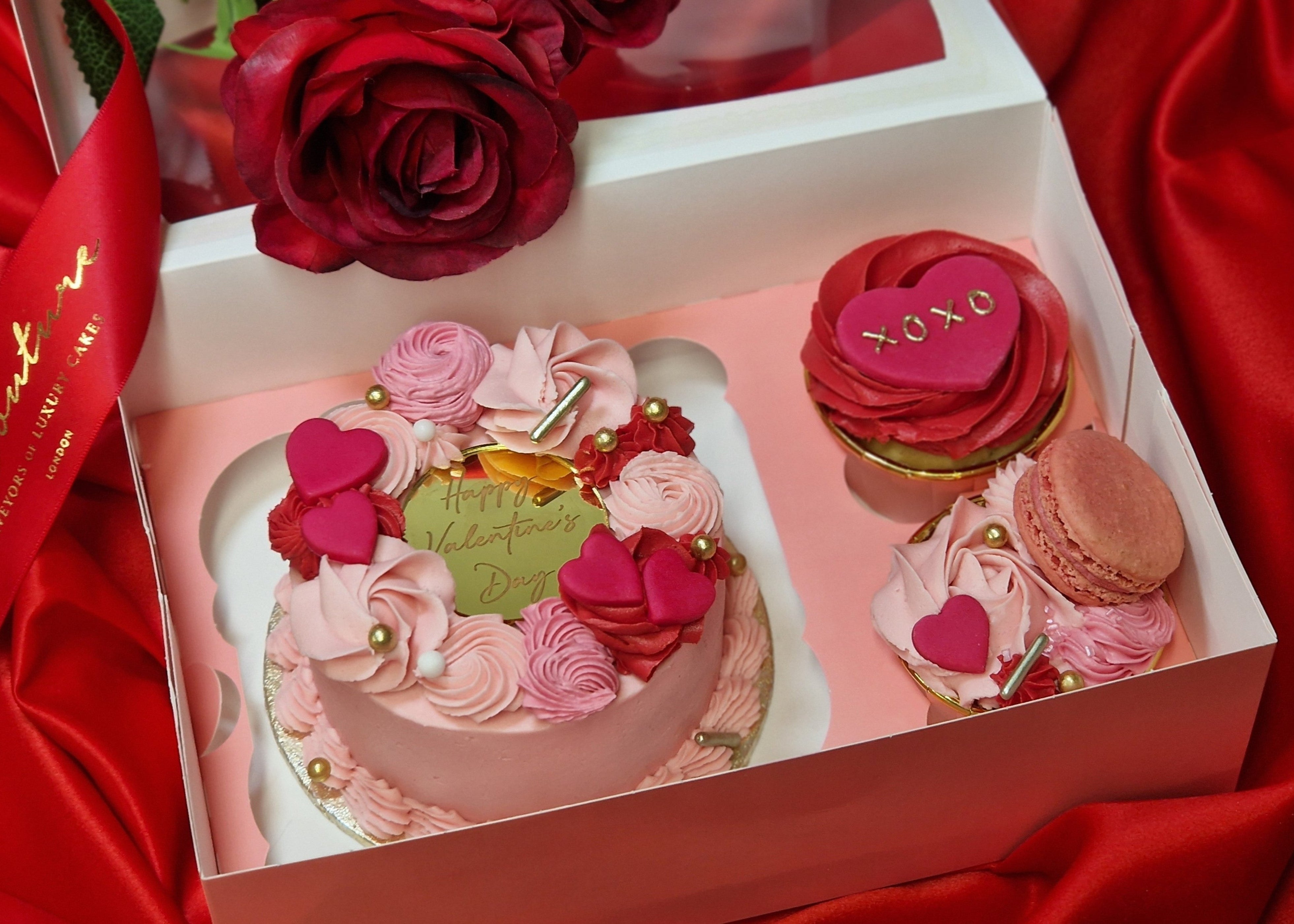 Valentine's Bento Box featuring a pink buttercream mini cake with heart decorations and buttercream swirls, accompanied by 2 cupcakes decorated with macaron, fondant hearts and gold sprinkles