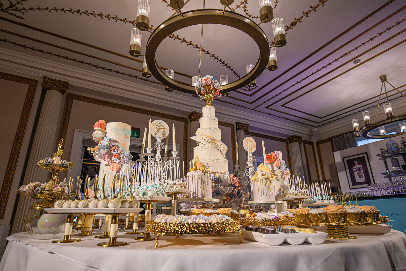 large round table showing big spread of bespoke indulgent luxury cakes and sweet deserts in a high class london hotel