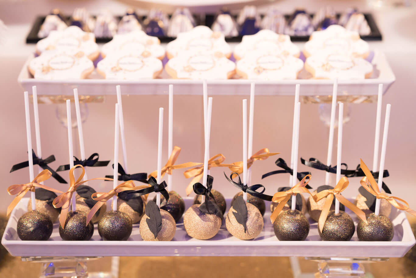 rows of luxurious black and gold cake pops, glitter, ribbon, feather icing