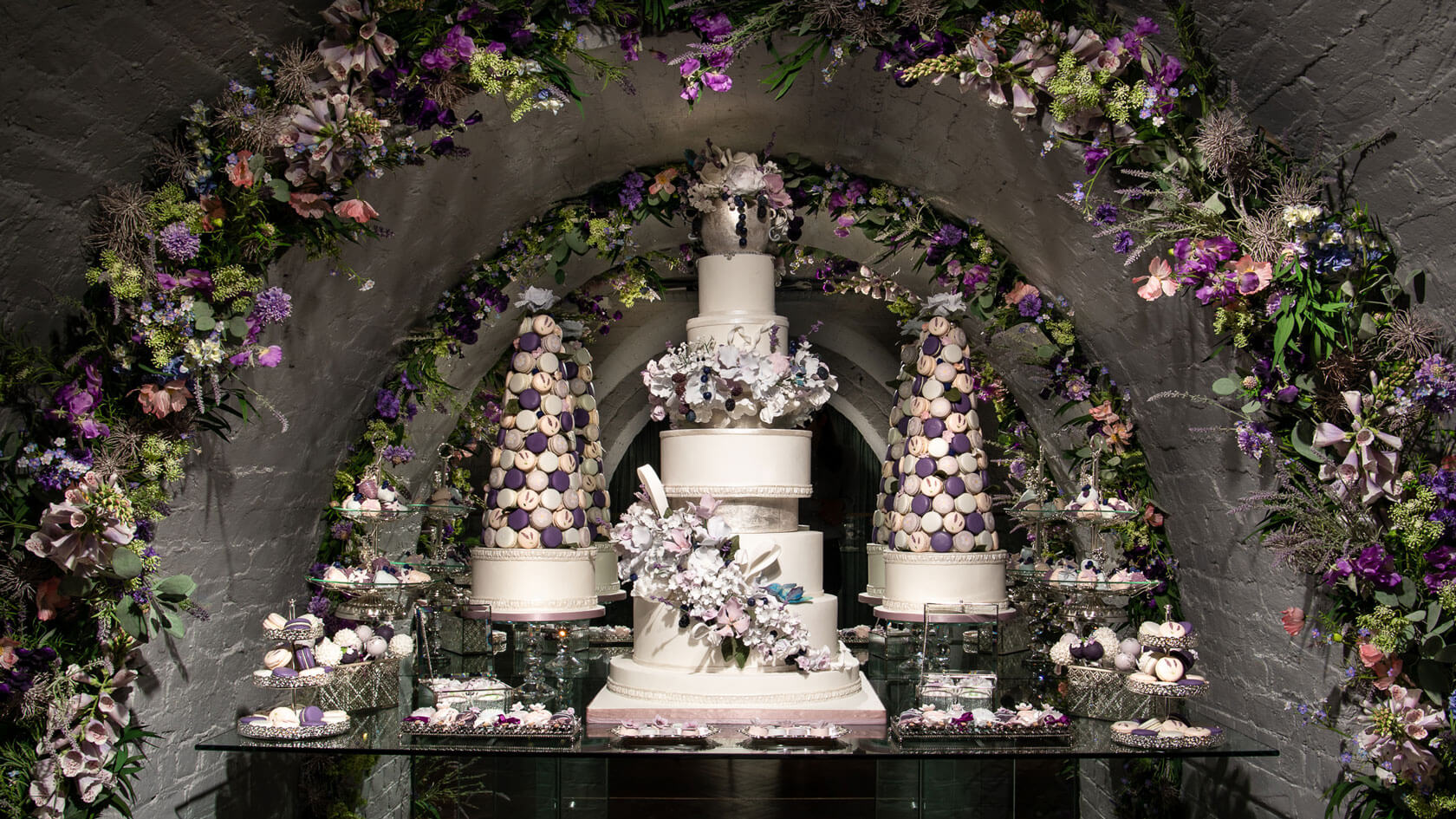 a bespoke luxury wedding cake surrounded by sweet treats and flowers in london