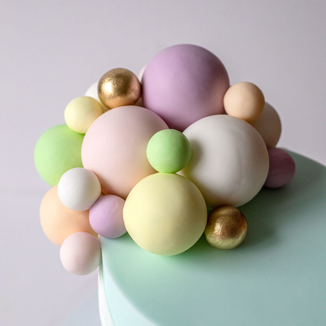 Birthday cake with a cluster of colourful balloons and a teddy bear holding onto balloon strings