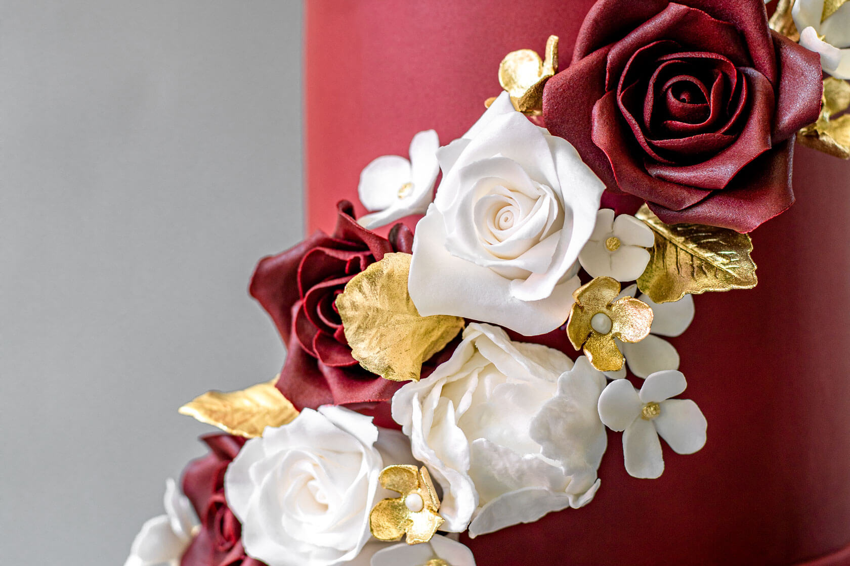 A three-tiered burgundy wedding cake decorated with cascading sugar flowers accented by gold leaves and blossoms