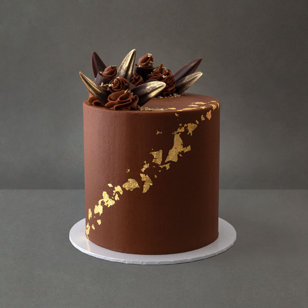 Delicious light and moist chocolate cake with 6 layers of buttercream filling. Gold leaf designs with chocolate decorations and chocolate buttercream swirls