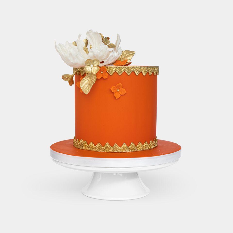 Luxurious orange fondant cake with gold lace detailing, large white peony with gold leaves topper