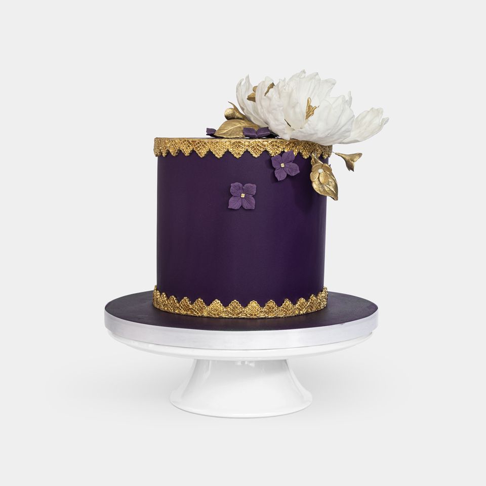 Luxurious purple fondant cake with gold lace detailing, large white peony with gold leaves topper