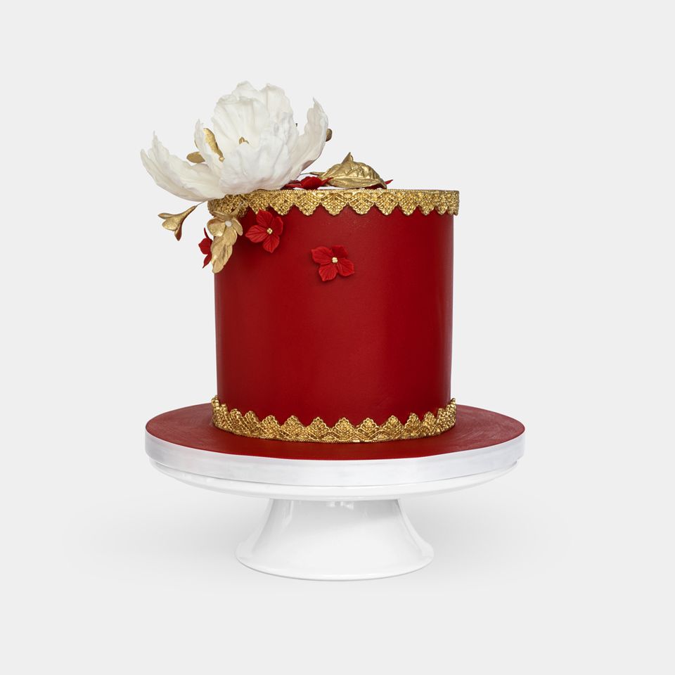 Luxurious red fondant cake with gold lace detailing, large white peony with gold leaves topper