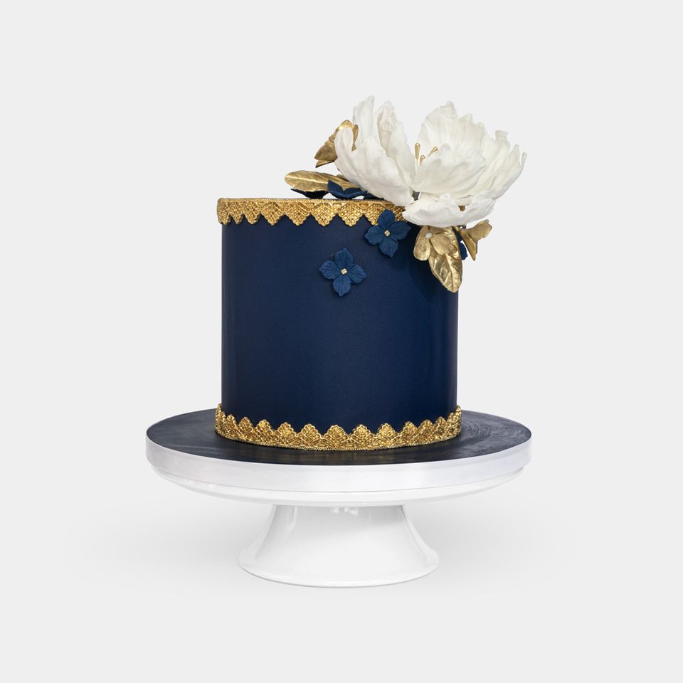 Luxurious navy fondant cake with gold lace detailing, large white peony with gold leaves topper