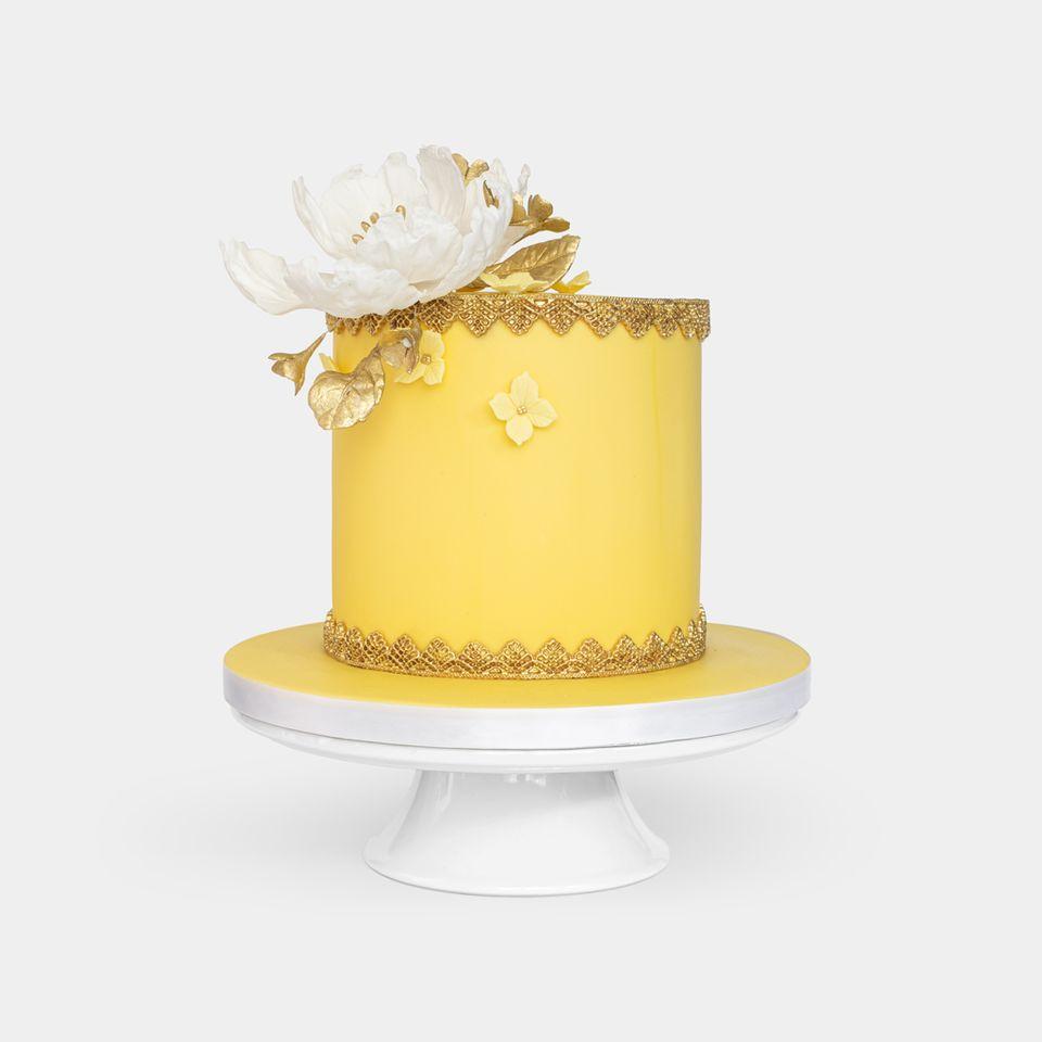 Luxurious yellow fondant cake with gold lace detailing, large white peony with gold leaves topper