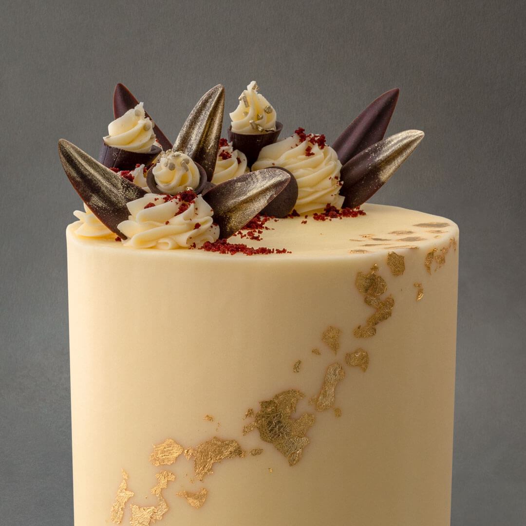 Light and moist gluten free red velvet cake with 6 layers of vanilla buttercream filling. Gold leaf designs with dark chocolate decorations and  vanilla buttercream swirls.