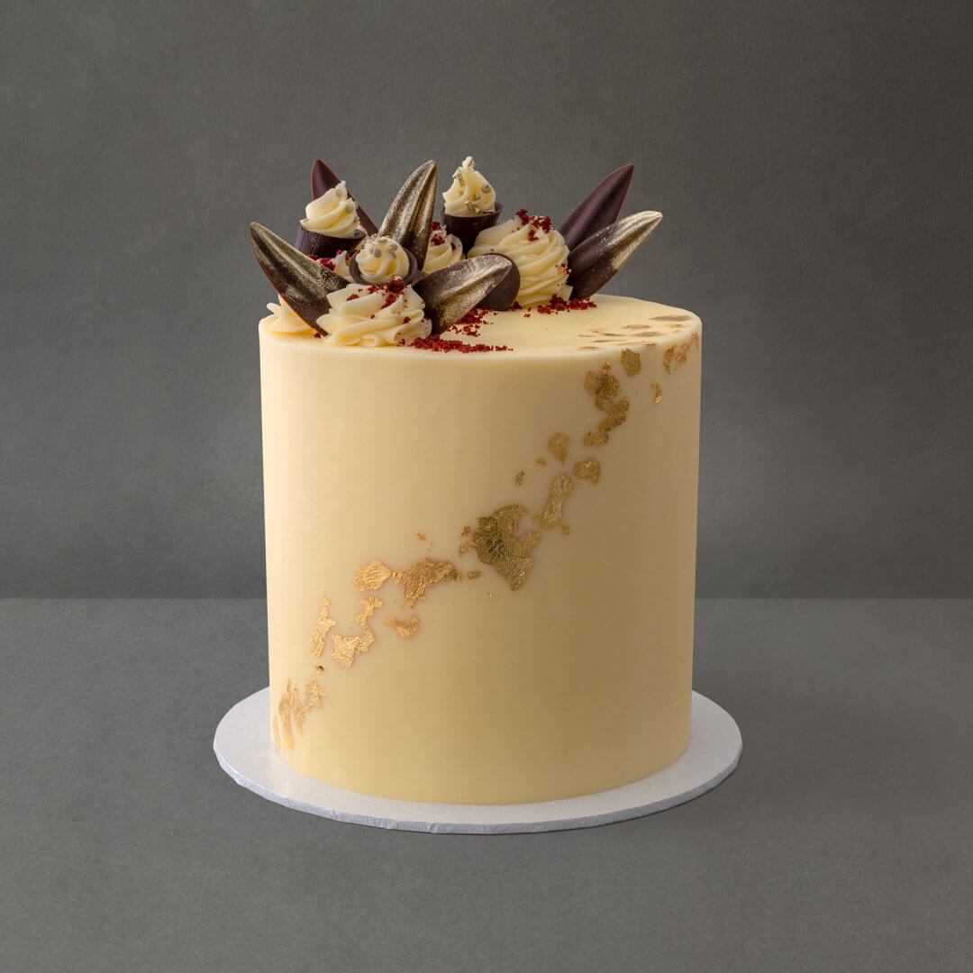 Light and moist gluten free red velvet cake with 6 layers of vanilla buttercream filling. Gold leaf designs with dark chocolate decorations and  vanilla buttercream swirls.