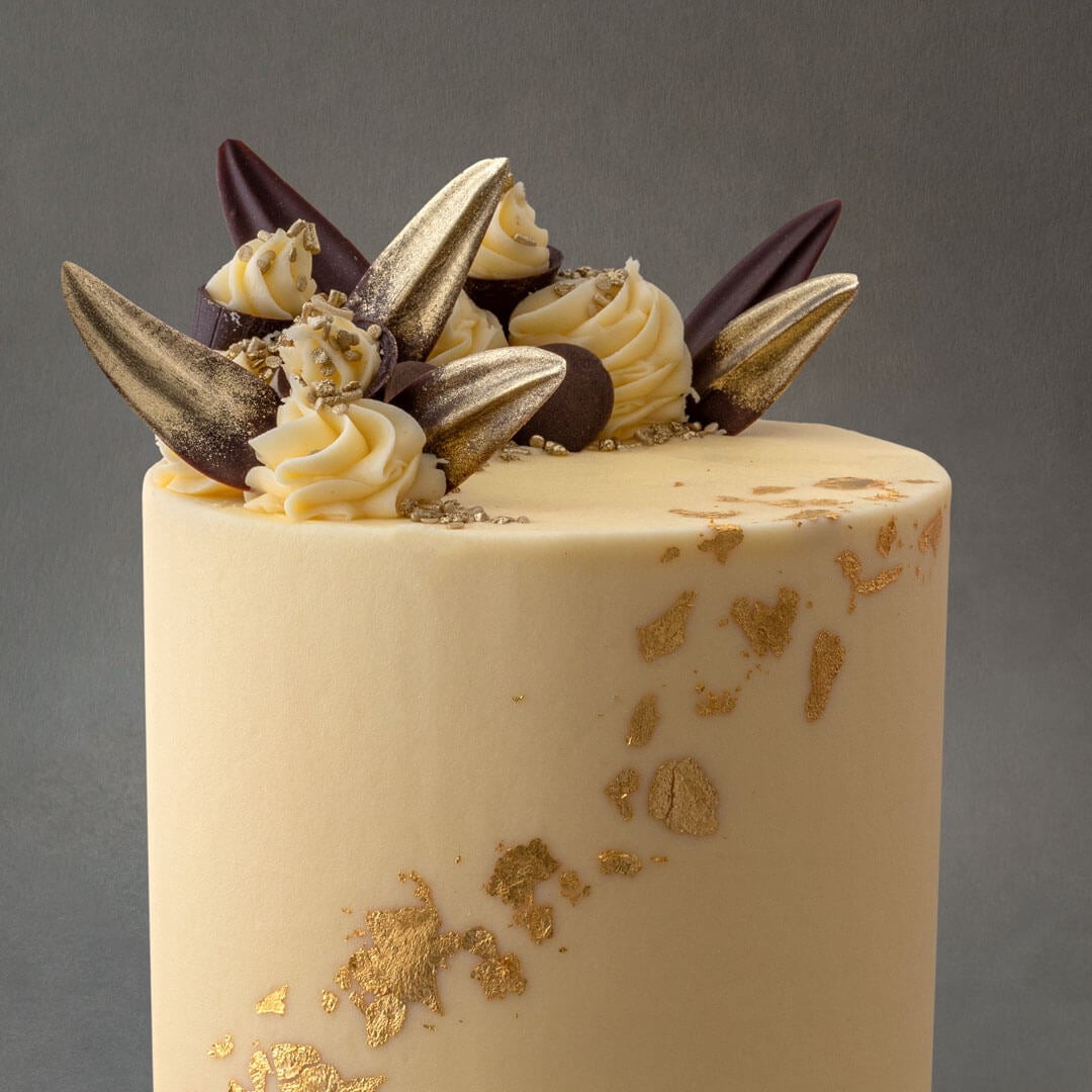 Delicious light gluten free vanilla sponge cake with 6 layers of vanilla buttercream filling. Gold leaf design with chocolate decorations and buttercream swirls.