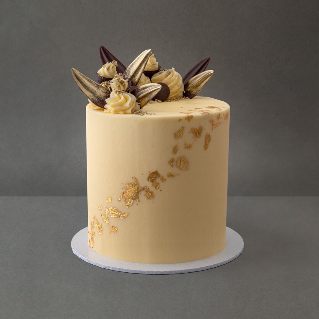 Delicious light gluten free vanilla sponge cake with 6 layers of vanilla buttercream filling. Gold leaf design with chocolate decorations and buttercream swirls.