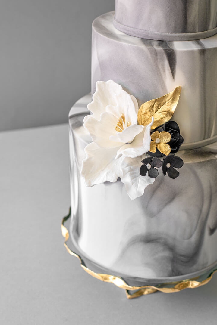 3-tier grey marble wedding cake with white sugar flowers and subtle black and gold accents