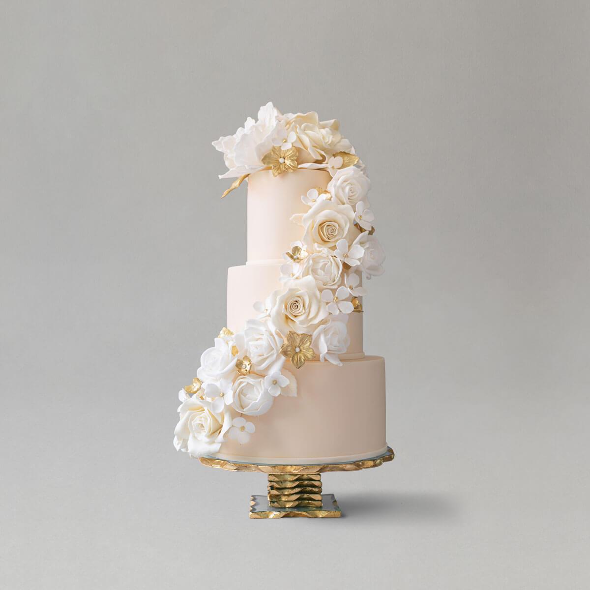 A three-tiered ivory wedding cake with white sugar flowers and gold accents