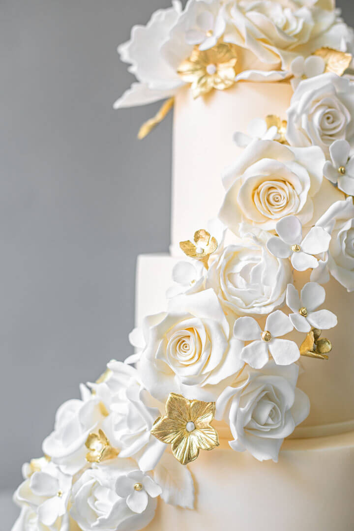 A three-tiered ivory wedding cake with white sugar flowers and gold accents