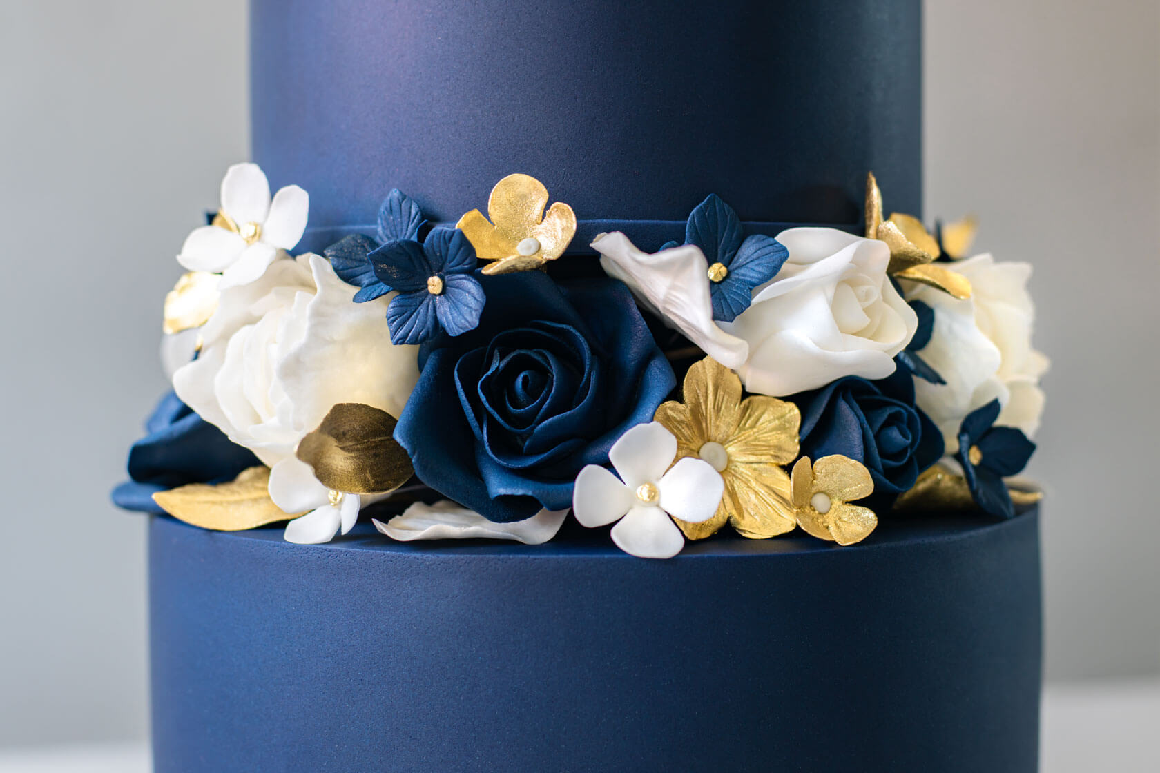 Elegant navy blue wedding cake with handmade sugar flowers between base tiers, topped with a large white handmade floral on the top