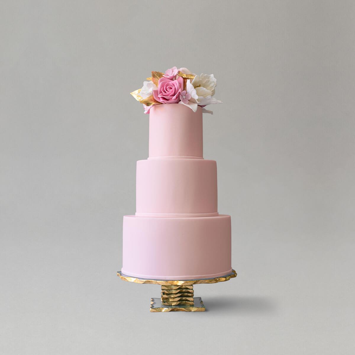 A 3 tiered pink wedding cake topped with handmade sugar flowers in pink, white and gold