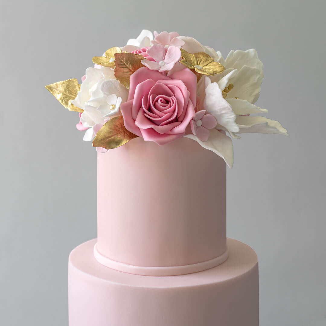 A 3 tiered pink wedding cake topped with handmade sugar flowers in pink, white and gold